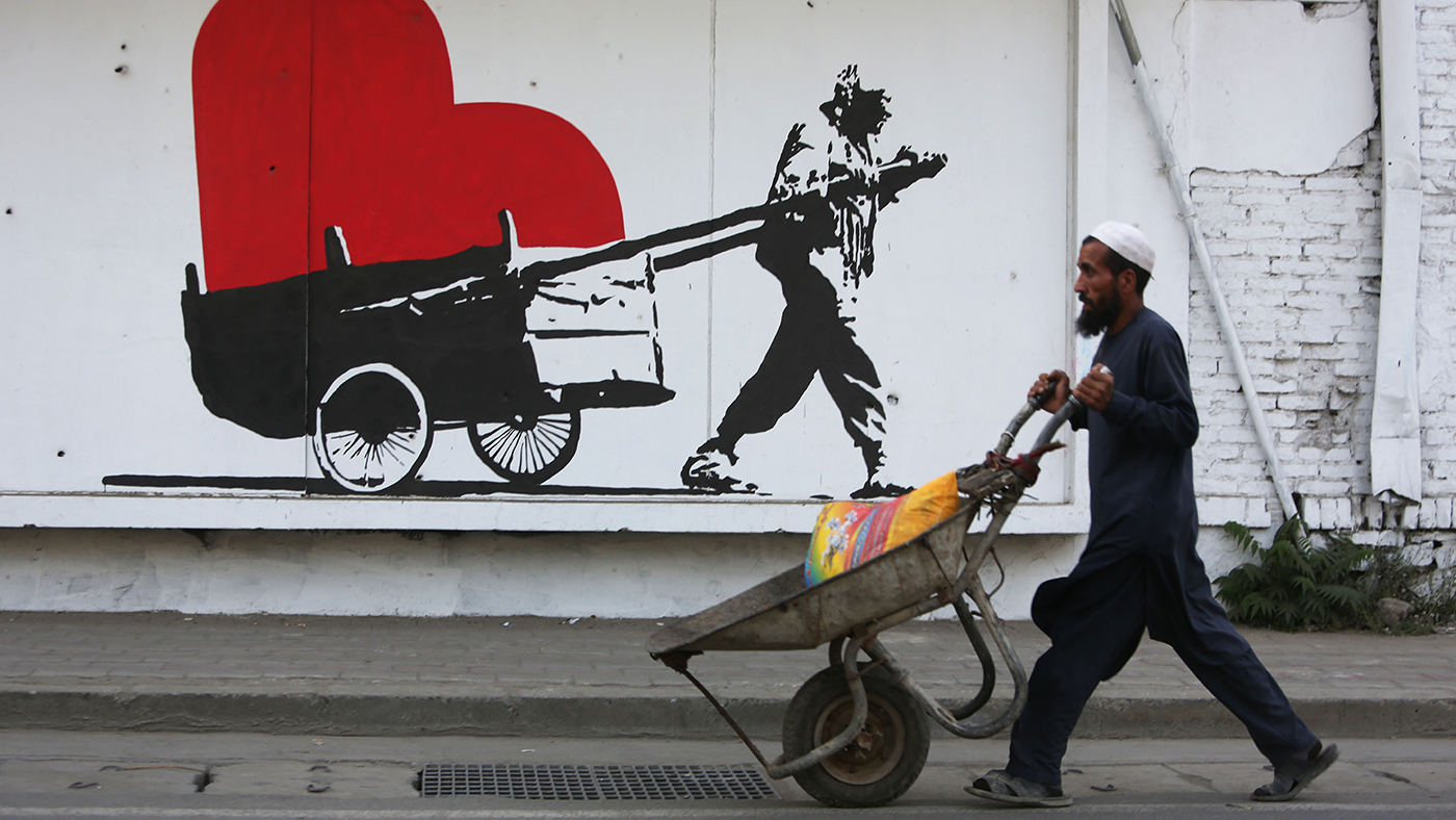 Afegão passa com carrinho de mão em frente a grafite que homenageia seu trabalho (AP Photo/Rahmat Gul)