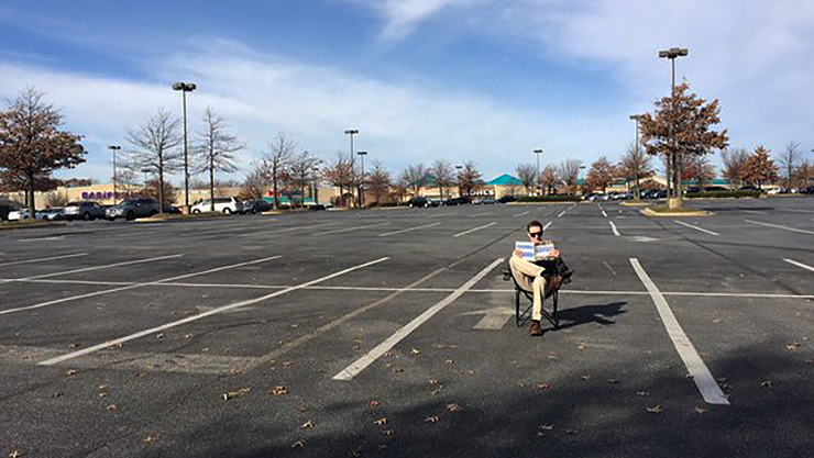Pessoa lê uma revista em estacionamento vazio durante a Black Friday (Twitter/Sean Emerson)