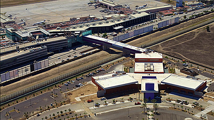 Vista aérea do Cross Border XPress, com a ponte passando sobre o muro da fronteira e o terminal do aeroporto em Tijuana à esquerda